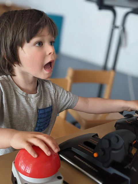 Junge hält einen Joystick und drückt einen roten Knopf und ist erstaunt